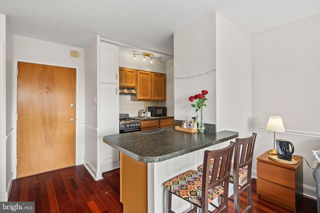 kitchen with dark wood-type flooring, high end range, a kitchen breakfast bar, kitchen peninsula, and decorative backsplash