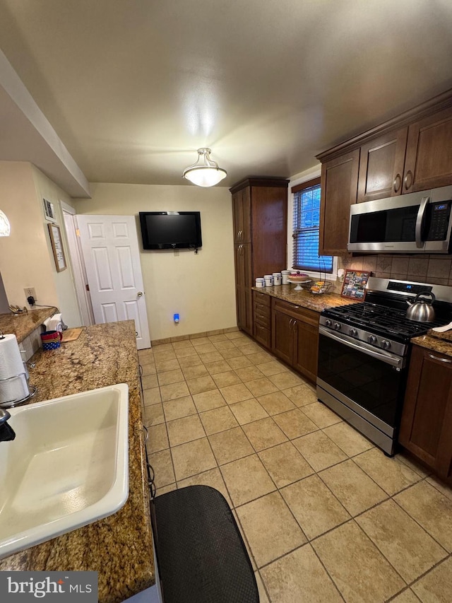 kitchen featuring dark brown cabinets, stainless steel appliances, light tile patterned floors, and sink