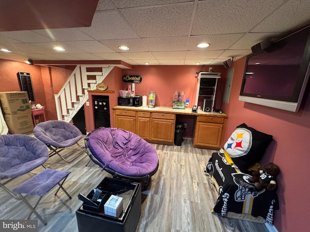 interior space with a paneled ceiling, light wood-type flooring, and indoor bar