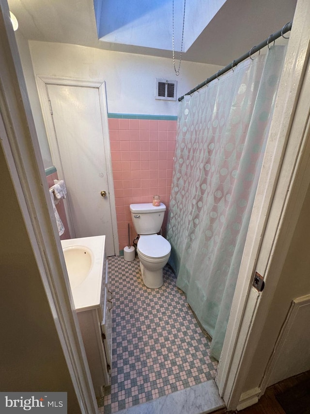 bathroom featuring vanity, toilet, and tile walls