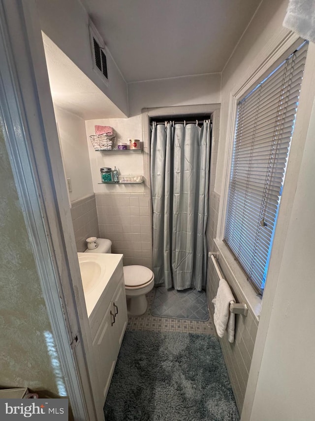 bathroom featuring tile patterned floors, vanity, toilet, and tile walls