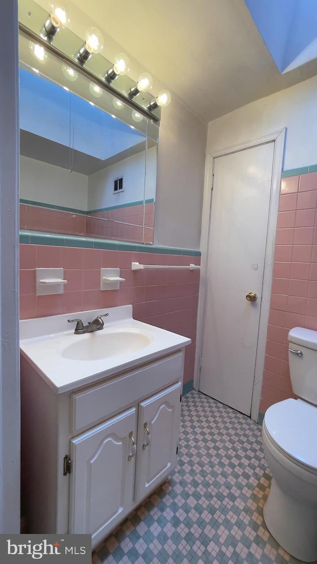 bathroom featuring vanity, toilet, and tile walls