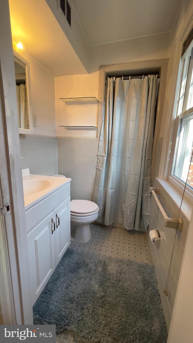 bathroom with vanity, toilet, and tile walls