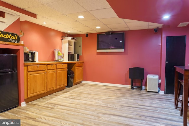 bar with light wood-type flooring, black fridge, and a drop ceiling