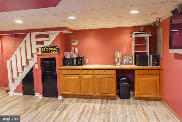 bar with light wood-type flooring, a drop ceiling, and black appliances