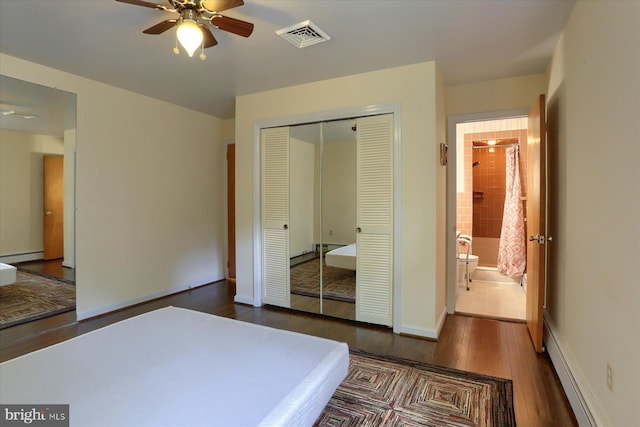 bedroom with ceiling fan, dark hardwood / wood-style floors, a baseboard radiator, a closet, and ensuite bath