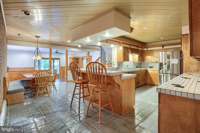 kitchen with tile counters, kitchen peninsula, stainless steel appliances, tile patterned floors, and pendant lighting