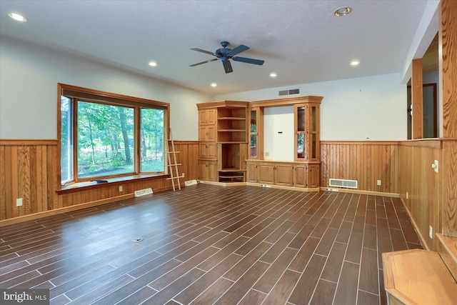 unfurnished living room featuring dark hardwood / wood-style flooring, ceiling fan, and wooden walls