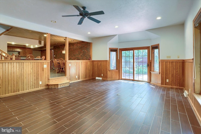 unfurnished living room with wood walls, dark hardwood / wood-style flooring, brick wall, and ceiling fan