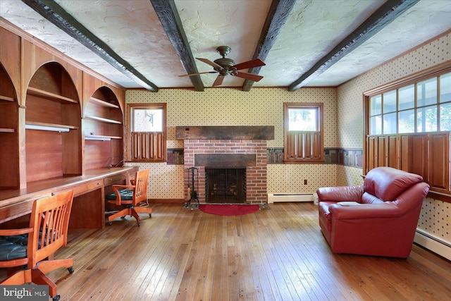 interior space featuring ceiling fan, beamed ceiling, baseboard heating, a brick fireplace, and wood-type flooring