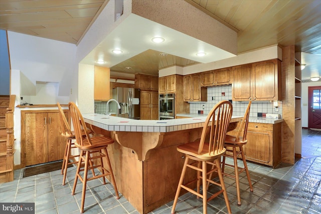 kitchen with tile patterned floors, stainless steel refrigerator with ice dispenser, tile counters, kitchen peninsula, and backsplash