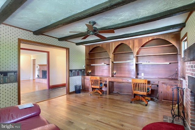 office featuring beamed ceiling, a brick fireplace, hardwood / wood-style flooring, and ceiling fan