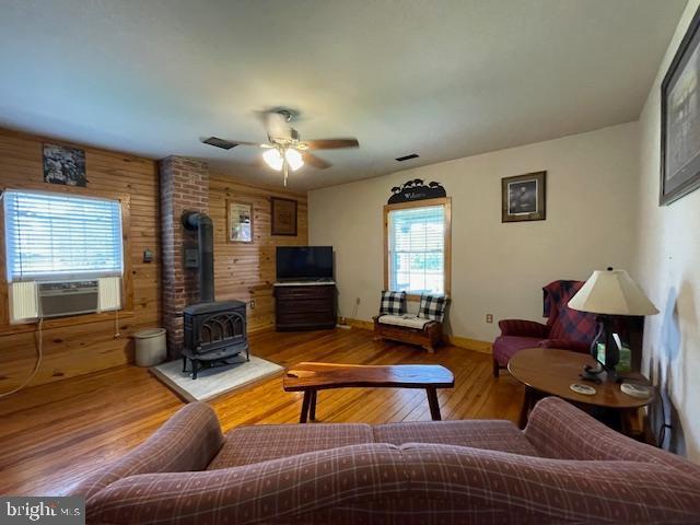 living room with wood walls, cooling unit, a wood stove, hardwood / wood-style flooring, and ceiling fan