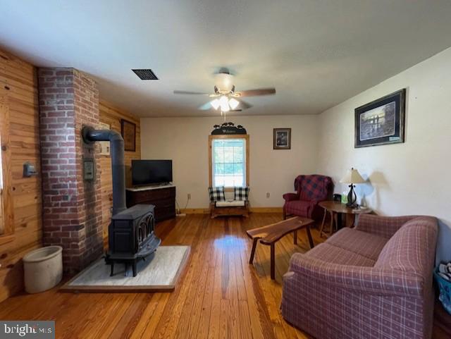 living room with hardwood / wood-style flooring, a wood stove, and ceiling fan