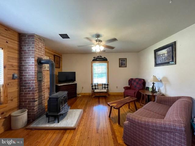 living room with wood-type flooring, a wood stove, and ceiling fan