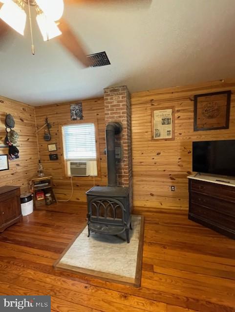 living room with cooling unit, hardwood / wood-style flooring, wooden walls, and a wood stove