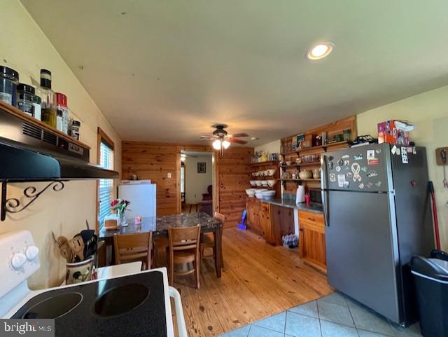 kitchen featuring ceiling fan, white appliances, light tile patterned floors, and wood walls