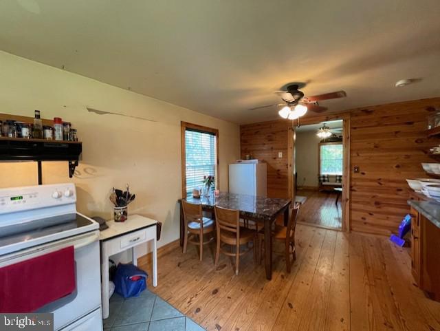 kitchen featuring hardwood / wood-style floors, white electric range, wooden walls, and plenty of natural light