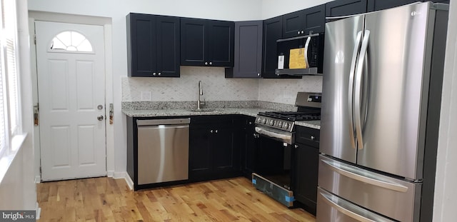 kitchen with light wood-type flooring, sink, backsplash, appliances with stainless steel finishes, and light stone countertops