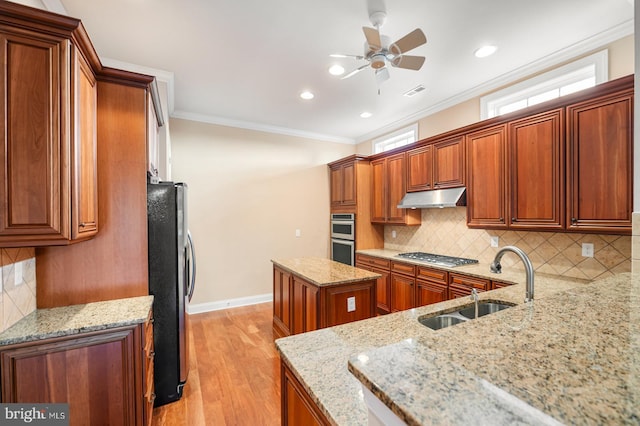 kitchen featuring sink, crown molding, stainless steel appliances, a center island, and light stone counters