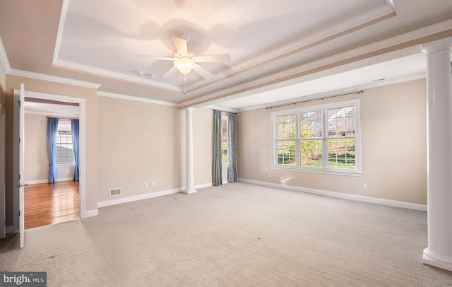 carpeted spare room with ceiling fan, ornamental molding, a tray ceiling, and decorative columns