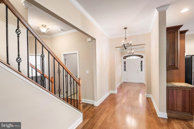 foyer entrance with an inviting chandelier, hardwood / wood-style flooring, ornamental molding, and a healthy amount of sunlight