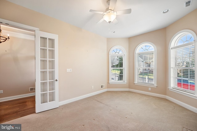 carpeted spare room with a healthy amount of sunlight and ceiling fan with notable chandelier