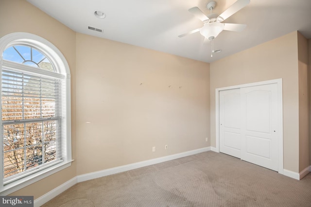 unfurnished bedroom featuring a closet, ceiling fan, light colored carpet, and multiple windows