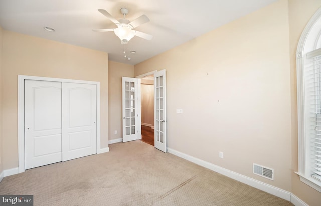 unfurnished bedroom featuring a closet, light colored carpet, french doors, and ceiling fan