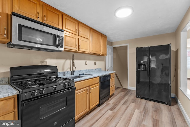 kitchen featuring sink, light stone counters, light hardwood / wood-style floors, and black appliances