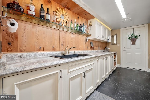 kitchen with sink, white cabinetry, light stone counters, and dark tile patterned flooring