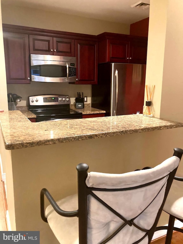 kitchen with light stone counters, a breakfast bar area, appliances with stainless steel finishes, and a peninsula