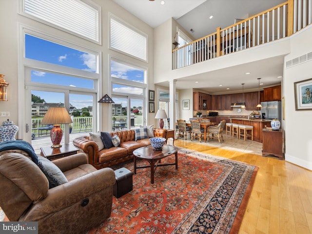 living room with decorative columns, a towering ceiling, and light hardwood / wood-style flooring