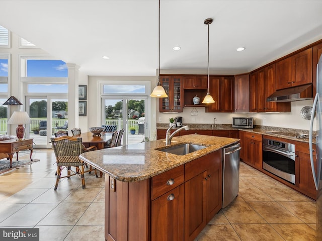 kitchen with sink, light stone counters, decorative light fixtures, an island with sink, and stainless steel appliances