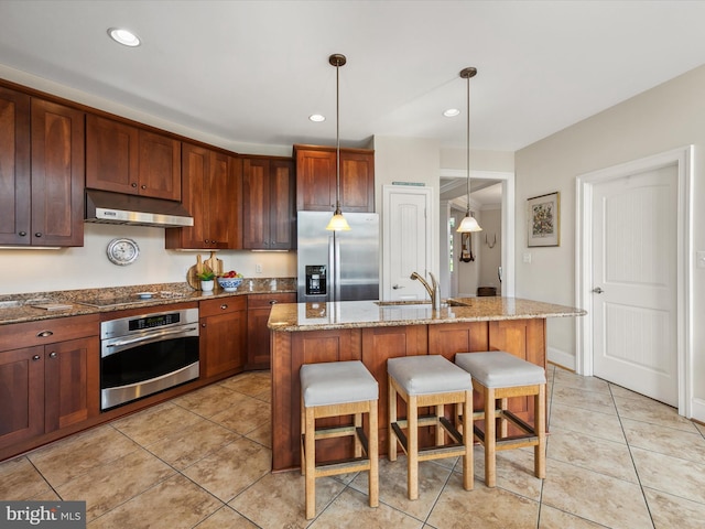 kitchen featuring appliances with stainless steel finishes, a breakfast bar, sink, a kitchen island with sink, and light stone countertops