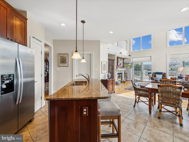 kitchen featuring stainless steel refrigerator with ice dispenser, sink, hanging light fixtures, a center island with sink, and a kitchen breakfast bar