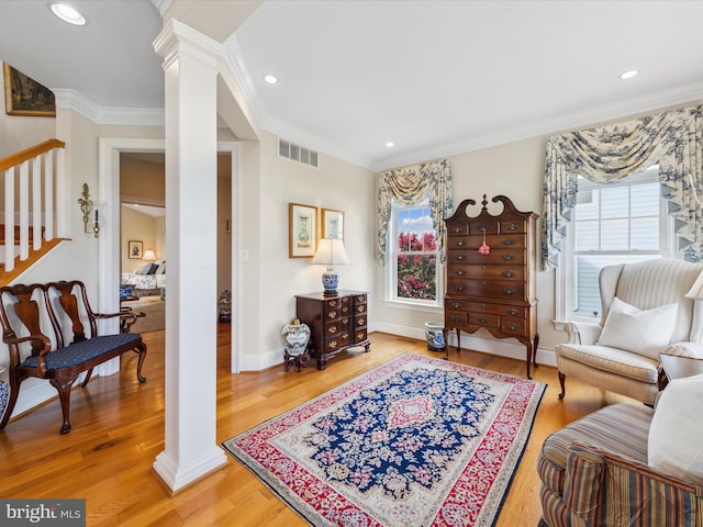 living area featuring decorative columns, crown molding, and wood-type flooring