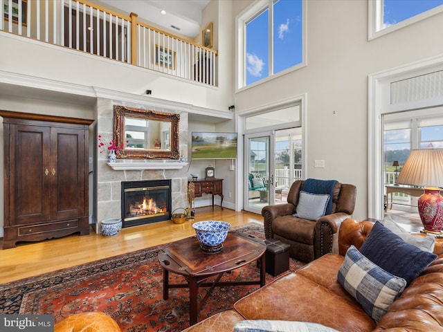 living room with a tiled fireplace, light wood-type flooring, and a high ceiling