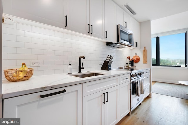 kitchen featuring sink, appliances with stainless steel finishes, backsplash, light stone countertops, and white cabinets