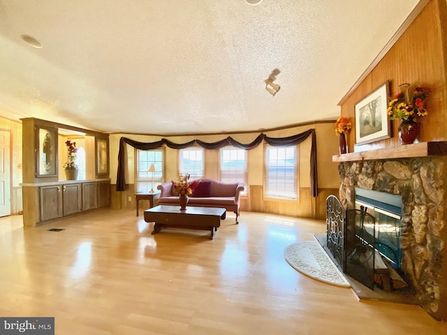 living room featuring ornamental molding, a fireplace, a textured ceiling, and wood walls