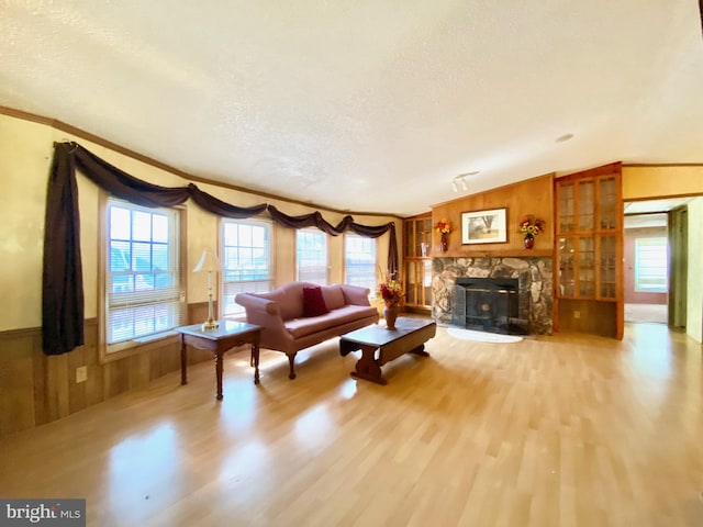 living room featuring lofted ceiling, wood walls, crown molding, a textured ceiling, and light hardwood / wood-style flooring