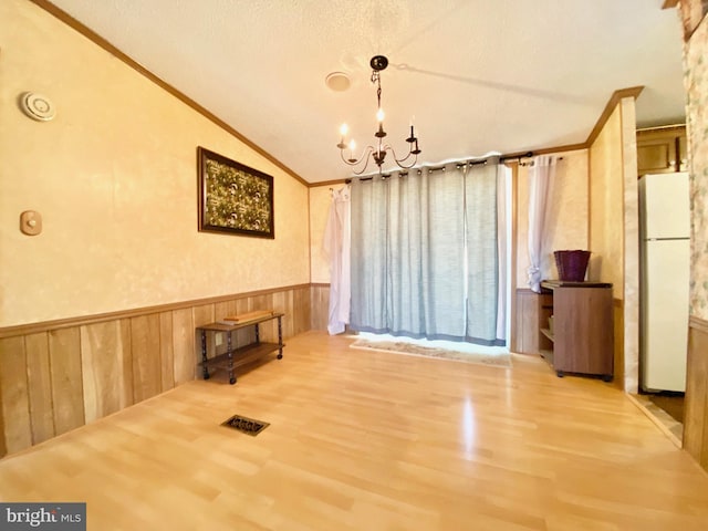 interior space with lofted ceiling, wood-type flooring, ornamental molding, and an inviting chandelier