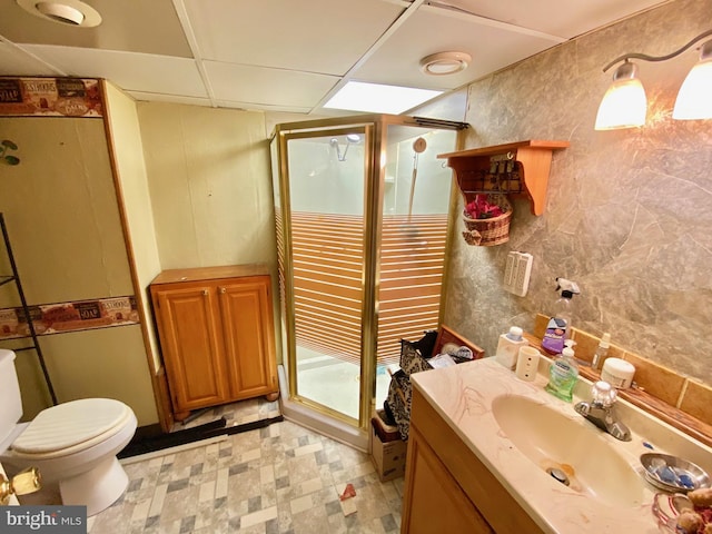 bathroom with a paneled ceiling, vanity, toilet, and a shower with door