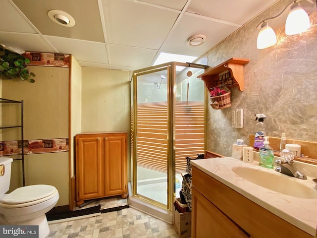 bathroom featuring vanity, toilet, a shower with shower door, and a drop ceiling