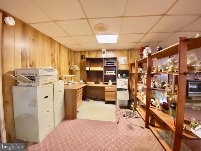 carpeted office space featuring a drop ceiling and wooden walls