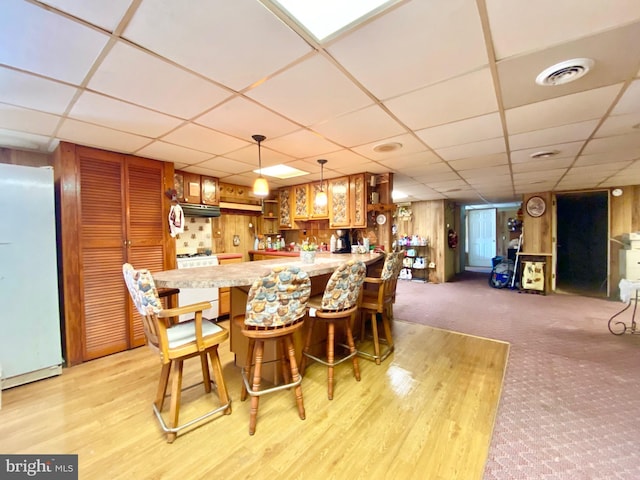 bar with white appliances, a paneled ceiling, decorative light fixtures, light colored carpet, and wood walls