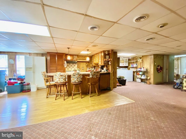 bar featuring light colored carpet, decorative light fixtures, a drop ceiling, and white fridge with ice dispenser