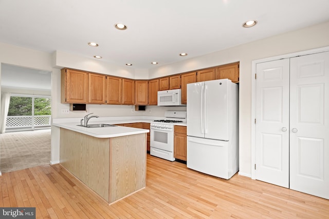 kitchen featuring sink, kitchen peninsula, white appliances, and light colored carpet