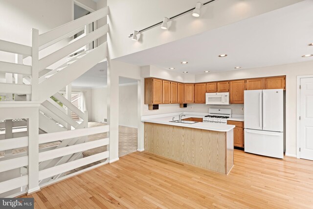 kitchen with white appliances, sink, kitchen peninsula, light hardwood / wood-style floors, and rail lighting