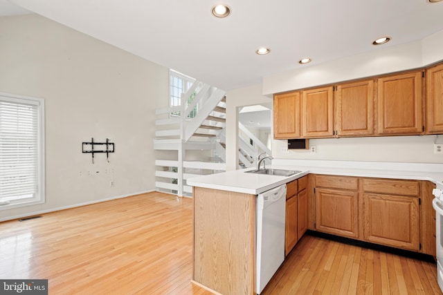 kitchen with sink, kitchen peninsula, light hardwood / wood-style flooring, and white appliances